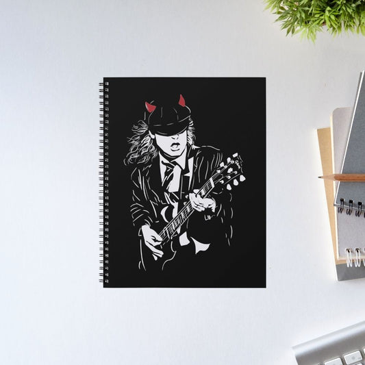 Notebook with a black cover featuring a stylized illustration of a person playing guitar on a white surface. AC/DC Notebook The Banyan Tee