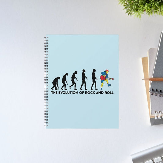 Notebook with 'The Evolution of Rock and Roll' design on a light blue cover, placed on a white surface. AC/DC Notebook The Banyan Tee
