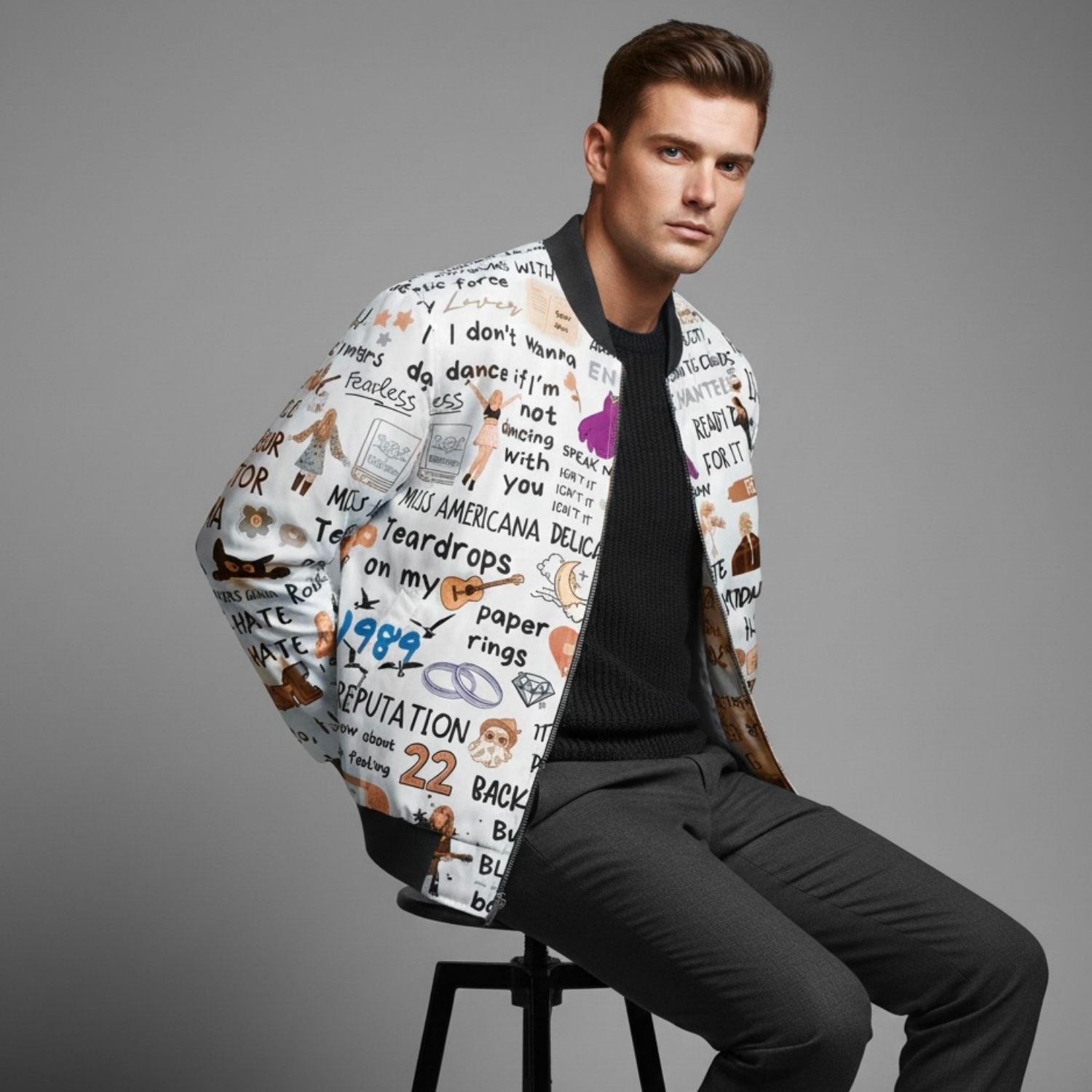 Man wearing a patterned Taylor Swift bomber jacket sitting on a stool against a gray background