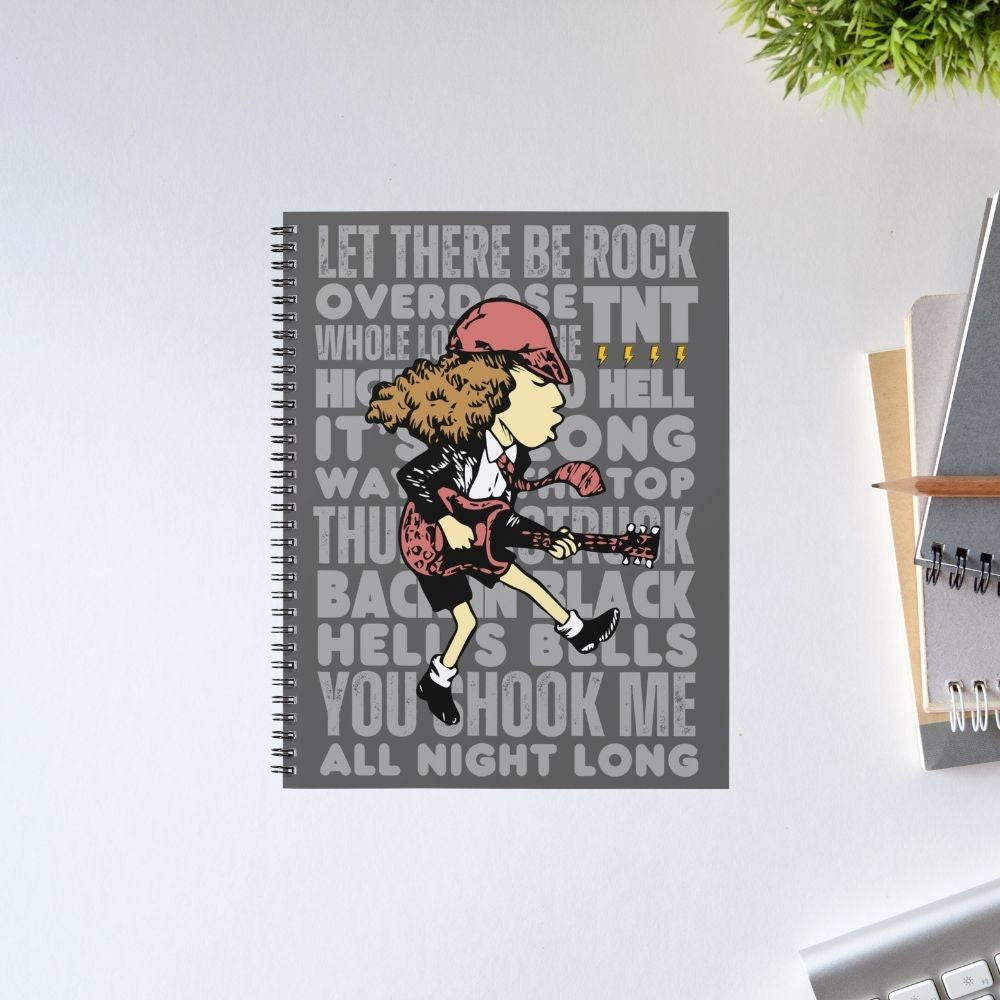Notebook with a graphic design of a person playing guitar and lyrics on a gray background, placed on a light surface. AC/DC Notebook The Banyan Tee