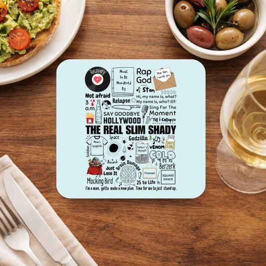 A square light blue coaster with a black and white 'The Real Slim Shady' rap lyrics graphic, displayed on a wooden dining table surrounded by food and a glass of white wine. eminem shady doodle coasters wooden table cups indian music band buy online india the banyan tee tbt men women girls boys unisex