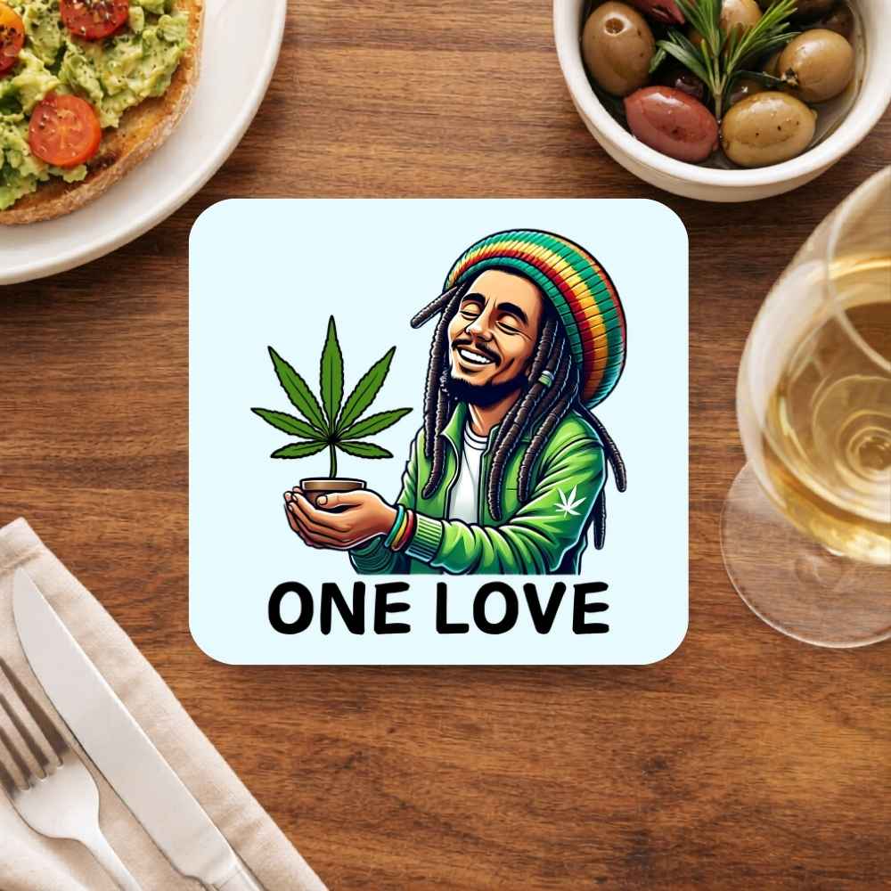 Coaster with a cannabis leaf and 'One Love' text on a table with food and drink. Bob Marley Gift Merch The Banyan Tee