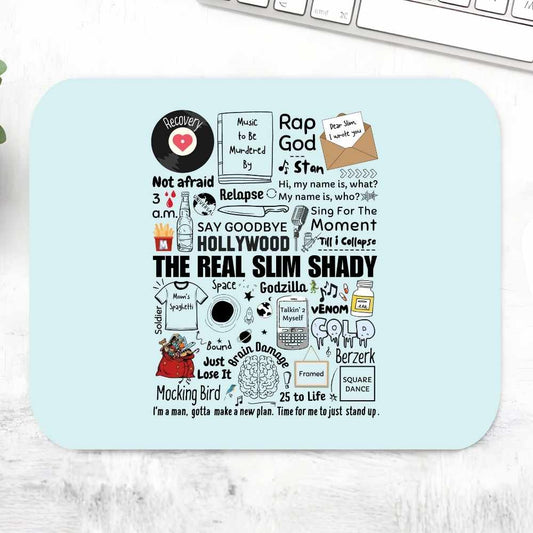 A rectangular light blue mouse pad with a black-and-white collage of slang, pop culture, and quote graphics, photographed on a white marble-like surface with part of a keyboard visible at the top. eminem shady doodle mousepad logitech large music band buy online united states of america usa the banyan tee tbt men women girls boys unisex