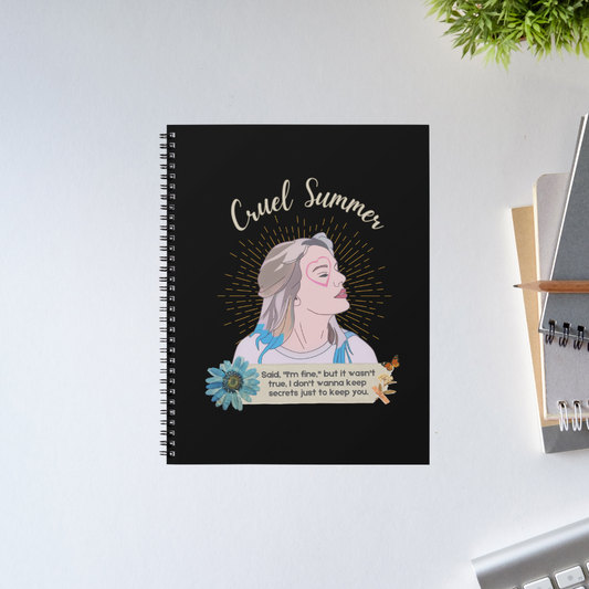 Taylor Swift Cruel Summer spiral notebook with a black cover, an illustrated profile portrait with a heart on her cheek, a blue daisy and a handwritten lyric strip – The Banyan Tee