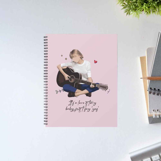 Taylor Swift Love Story spiral notebook with an illustrated guitarist and the lyric "It's a love story, baby, just say yes" on a pink cover – The Banyan Tee